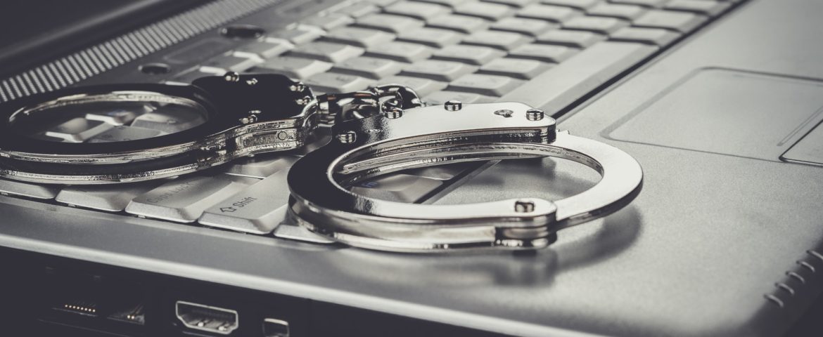 handcuffs on laptop cyber crime concept
